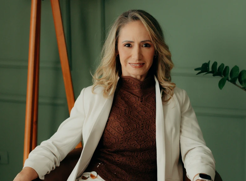 Dra. Anna Carolina sentada no consultório, de blazer branco